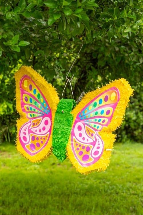 A butterfly piñata hanging in a tree that is for a bridal party.