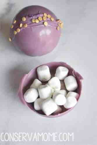 The inside of a chocolate bomb with hot cocoa mix and marshmallows. It is also purple with sprinkles on it.